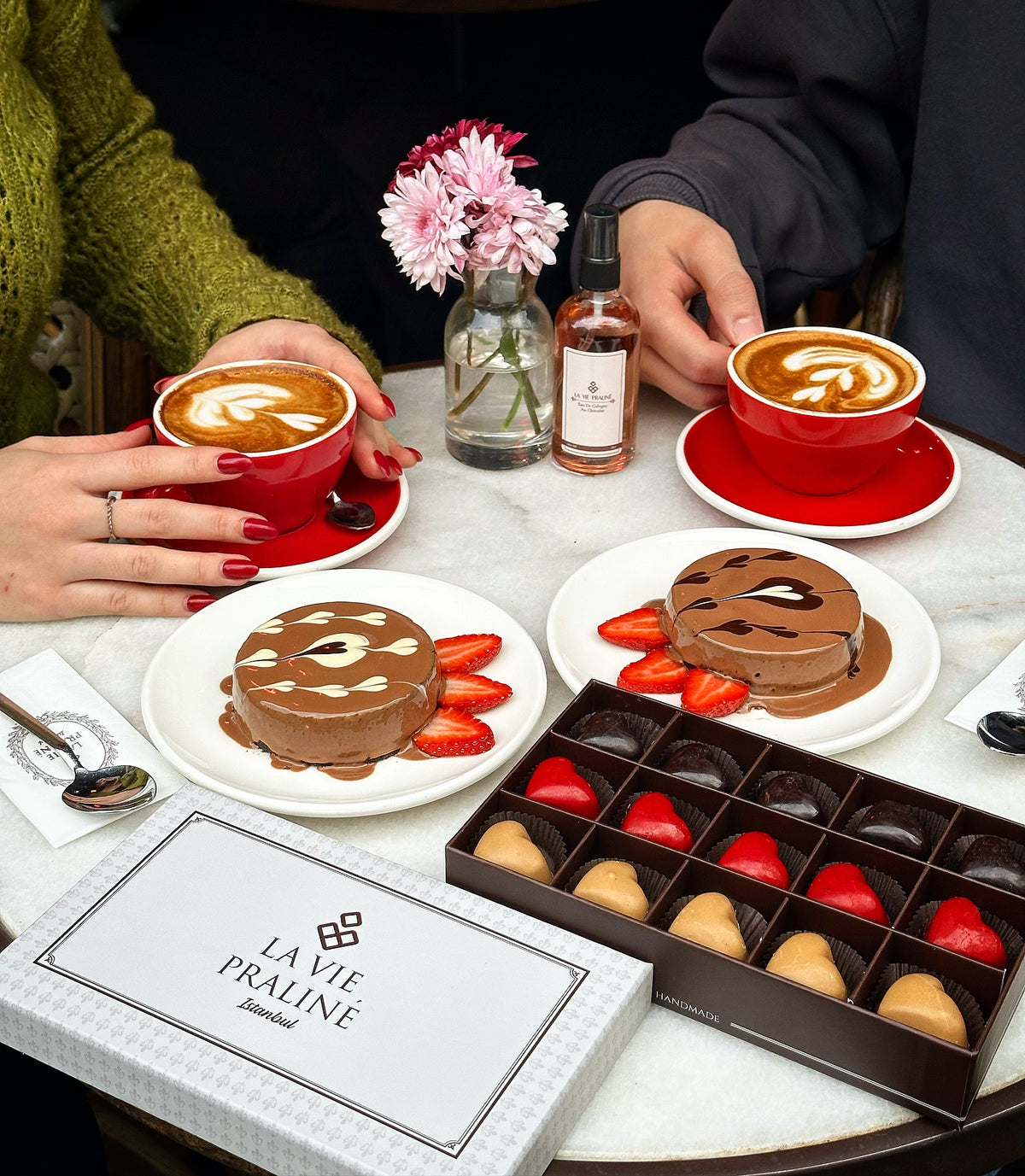Kafe masasında iki fincan kahve, çikolatalı tatlılar ve pralin kutusu